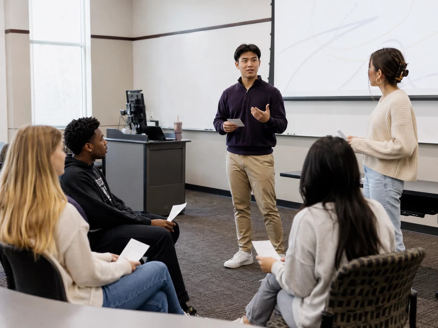 Students rehearsing a presentation in a classroom.